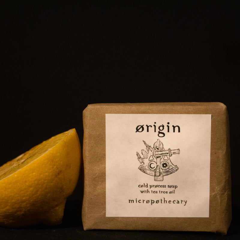 Micropothecary Origin cold process soap with tea tree and lemongrass beside fresh lemon on dark background